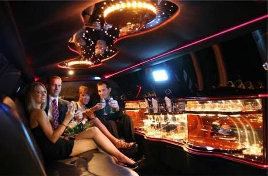 Four friends toasting with champagne inside a limousine with accent lighting and a lit bar
