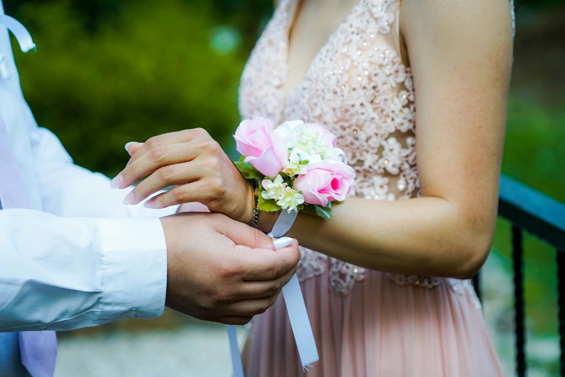 Prom date tying a pink rose corsage onto a wrist
