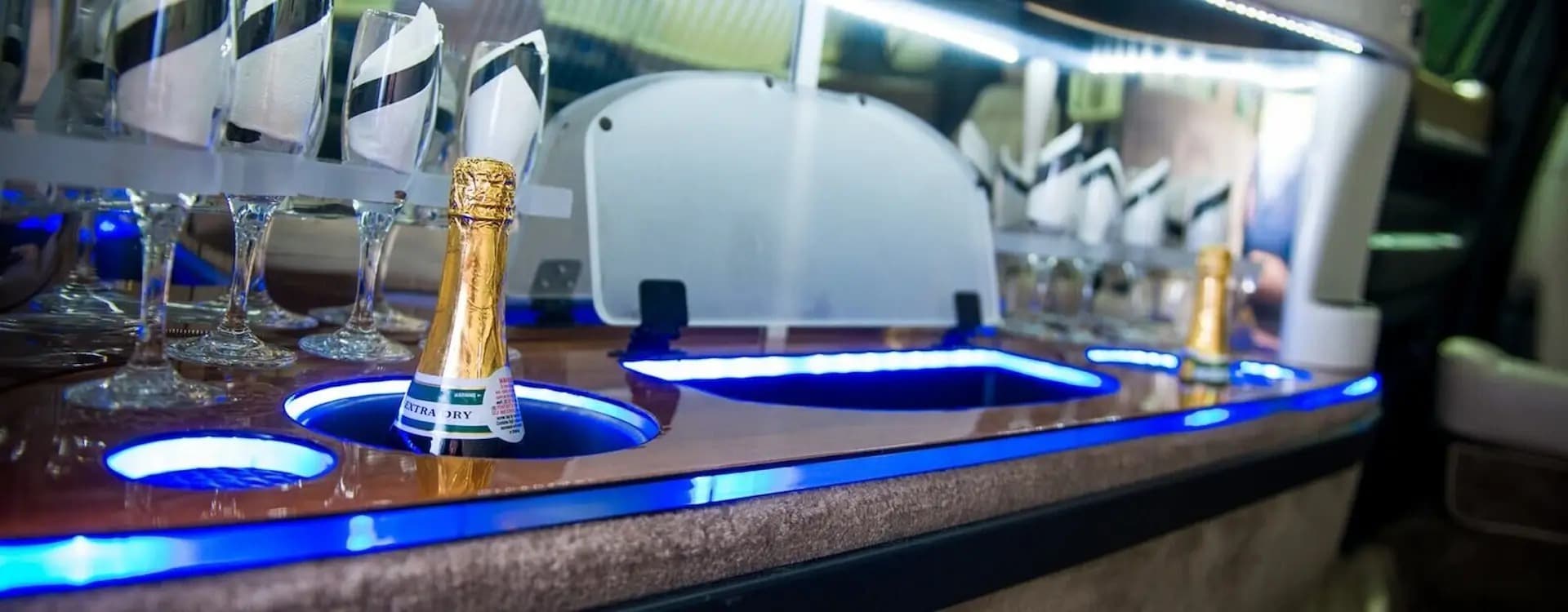 Champagne bottles and glasses at the bar of a limousine with blue accent lighting